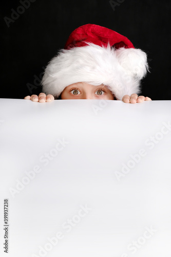 Boy in Santa's hat holding the white blank billboard  for christmas greetings. Isolated on black