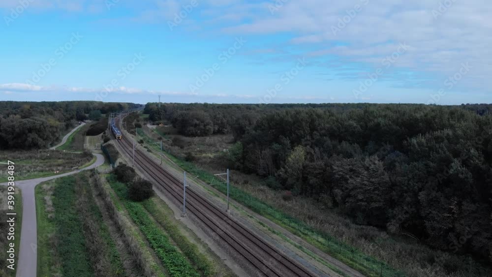 Dutch train passing on a railway track on a summer day in the netherlands, Drone shot Dutch train passing on a railway track on a summer day in the netherlands, Drone shot