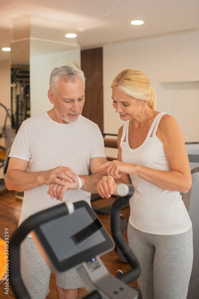 Mature couple checking pulsometers in gym and discussing the results Mature couple checking pulsometers in gym and discussing the results