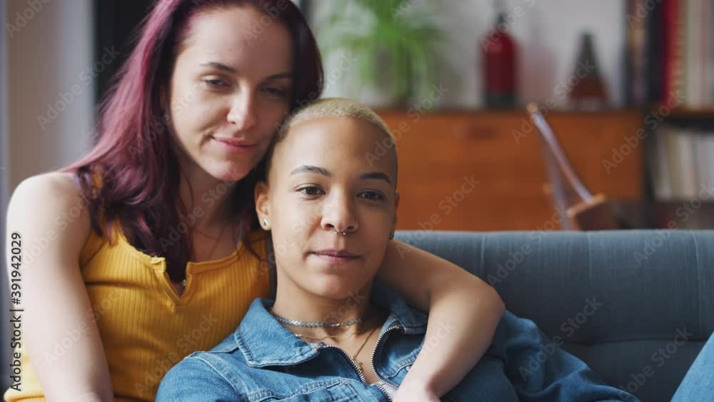 Loving same sex female couple hugging as they lie on sofa at home watching TV and relaxing together - shot in slow motion Loving same sex female couple hugging as they lie on sofa at home watching TV and relaxing together - shot in slow motion