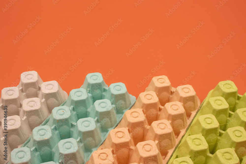 Multicolored organic egg trays on orange background with copyspace for your text. Biodegradable and compostable paper packaging. Waste sorting at home concept