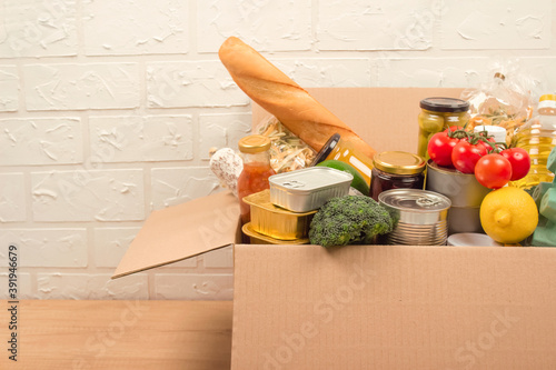 Donation box with different groceries, food donations on light background with copyspace - pasta, fresh vegatables, canned food, baguette, cooking oil. Food bank, food delivery concept