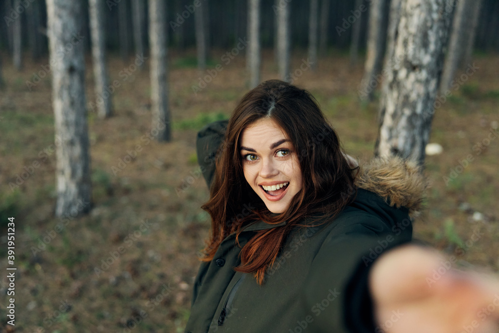 Cheerful woman in warm jacket in nature with outstretched hand on the background of the autumn forest