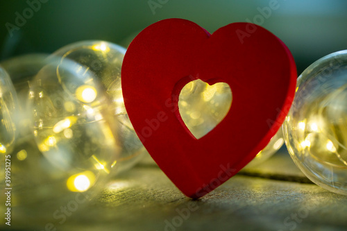 decorative red heart illuminated by a garland on a wooden surface