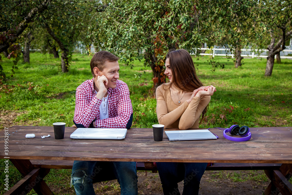 Naklejka premium A guy with a girl working on laptops in the park