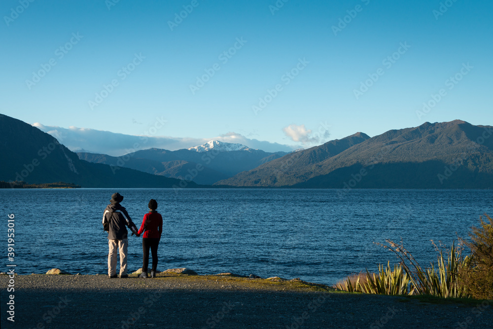 Couple enjoying the views of snow-capped mountains at Lake Brunner, South Island, New Zealand