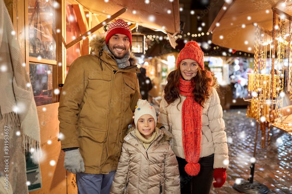 family, winter holidays and celebration concept - happy mother, father and little daughter at christmas market on town hall square in tallinn, estonia over snow