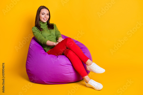 Photo of attractive lady sit comfortable violet bean bag wear green sweater red pants white sneakers isolated yellow color background