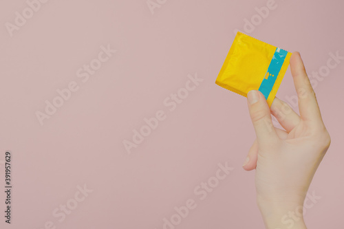 Hand holding a condom isolated on a ping background.Safe sex concept