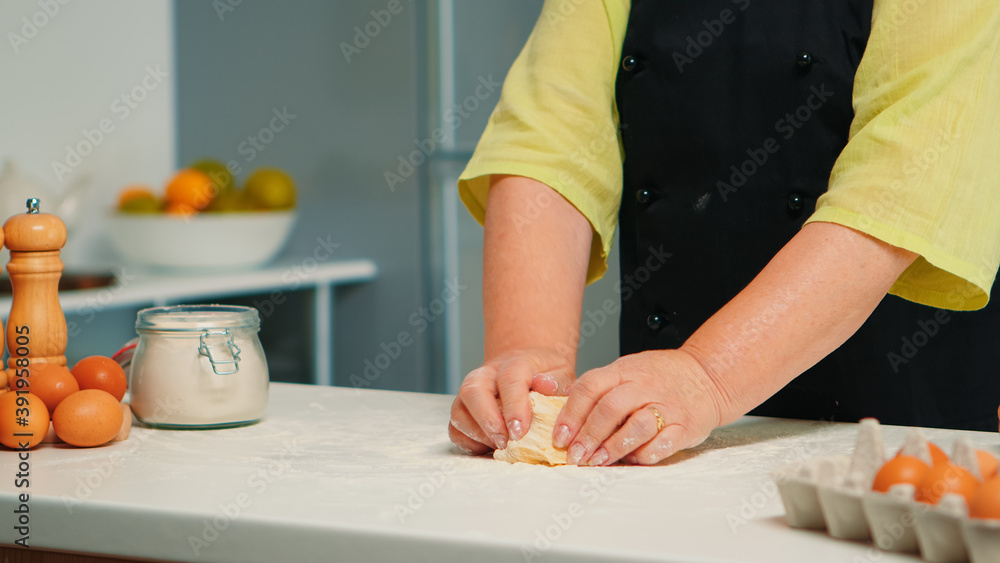 Baker preparing fresh breads and cakes at home in modern kitchen. Retired elderly baker with bonete mixing ingredients with wheat flour kneading dough for baking homemade cake and bread Baker preparing fresh breads and cakes at home in modern kitchen. Retired elderly baker with bonete mixing ingredients with wheat flour kneading dough for baking homemade cake and bread