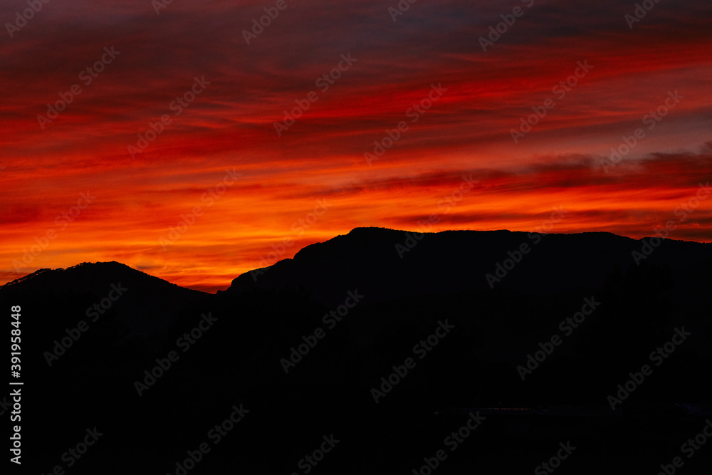 Scarlet summer sunset sky and dark mountains silhouette. Sundown clouds with dark mountains.