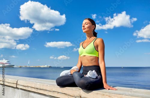 fitness  sport and yoga concept - young woman meditating in lotus pose at seaside