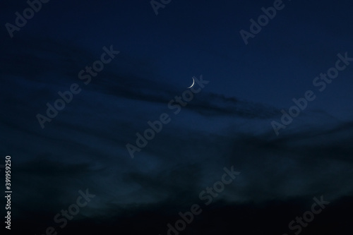 Sickle of the moon in the dark evening clouds. Night photo with the moon and clouds. Moonlight and dark summer clouds.