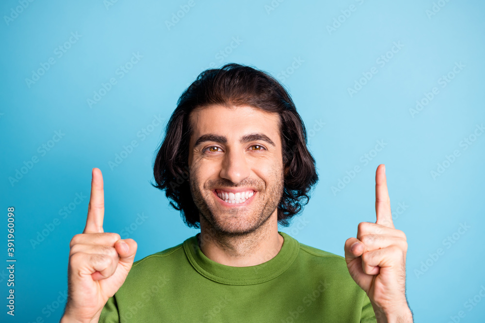 Close up portrait of satisfied person smile pointing two finger up green pullover isolated on blue color background Close up portrait of satisfied person smile pointing two finger up green pullover isolated on blue color background