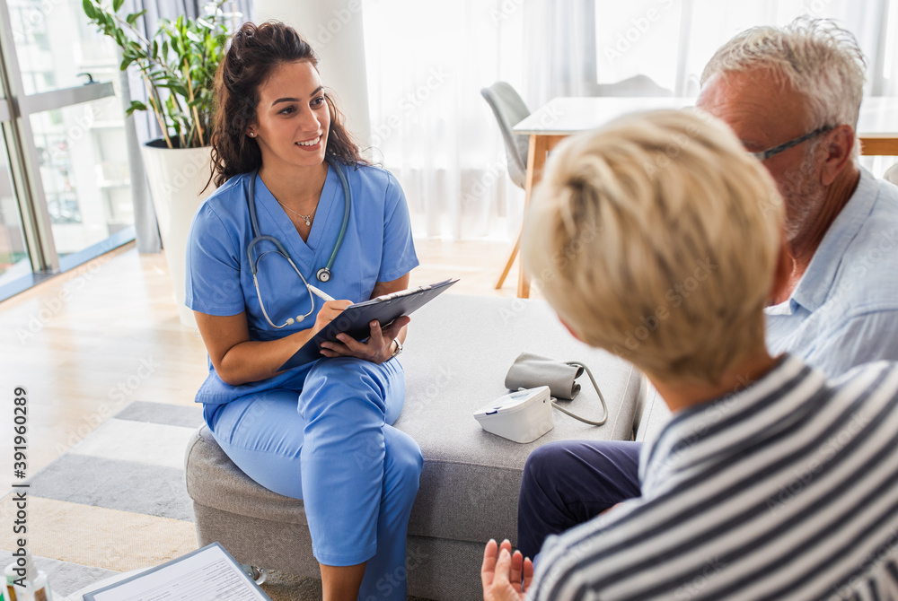 Fototapeta premium Female nurse talking to seniors patients while being in a home visit, senior couple signs an insurance policy. 