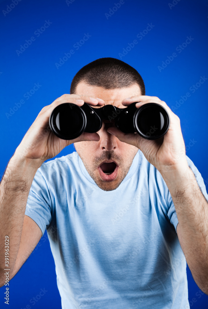 Naklejka premium Man with dark short hair looking through binoculars with a surprised look.