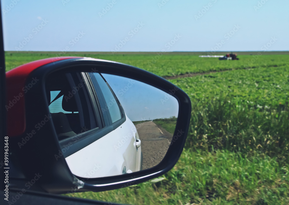 Espejo retrovisor de un coche circulando por una carretera rural. Vista borrosa por efecto de la velocidad de los campos de cultivo del sur de Rumanía.