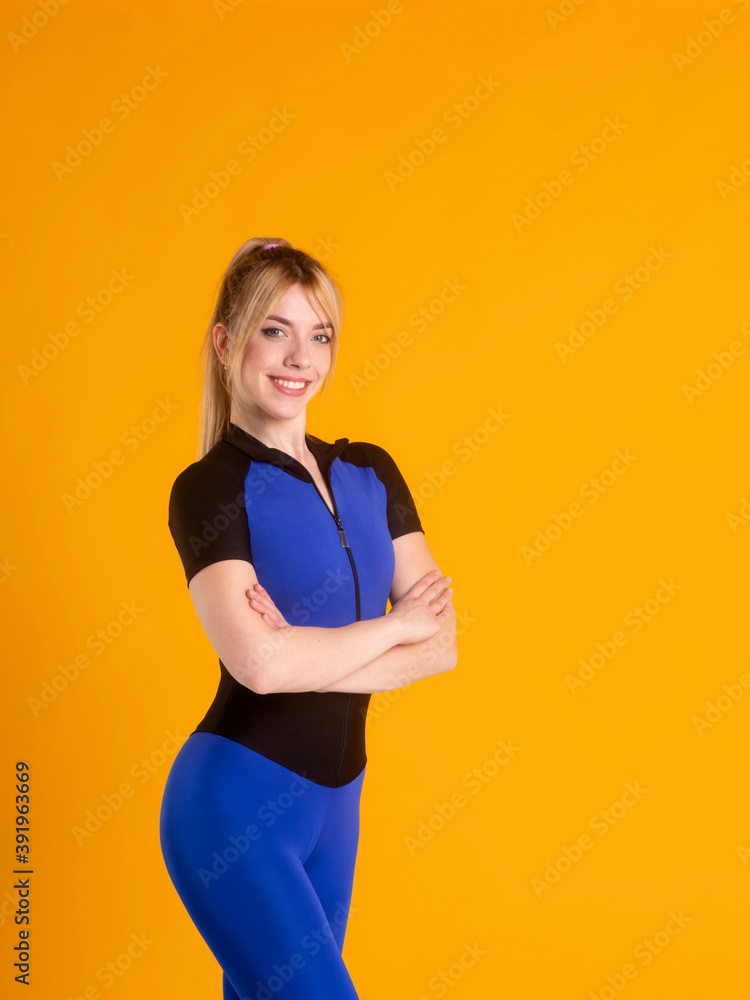 girl fitness trainer in a blue jumpsuit on a yellow background a Young athlete poses and looks at the camera and smiles. girl fitness trainer in a blue jumpsuit on a yellow background a Young athlete poses and looks at the camera and smiles.