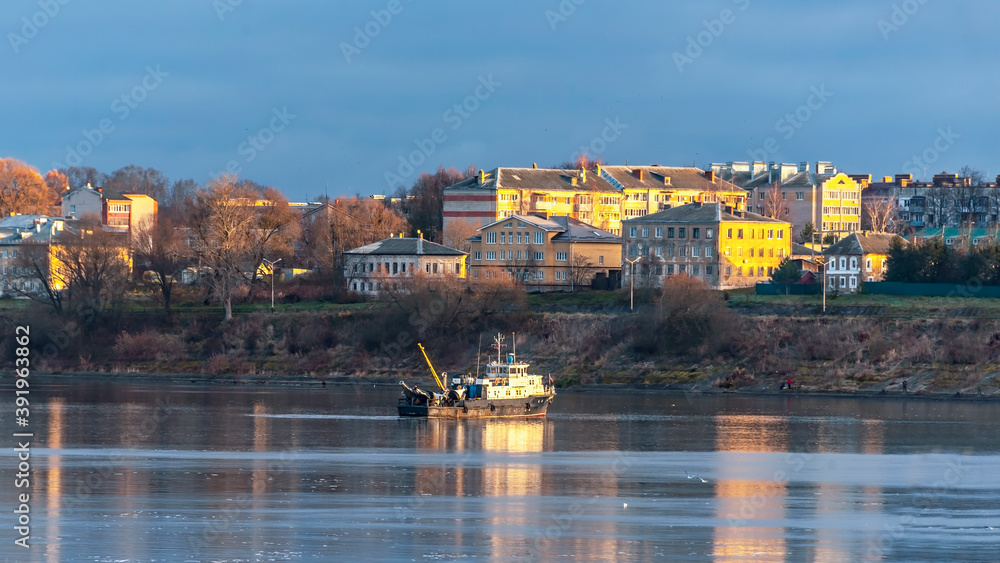 Tug ship on the river against the background of the cityscape at sunrise.
