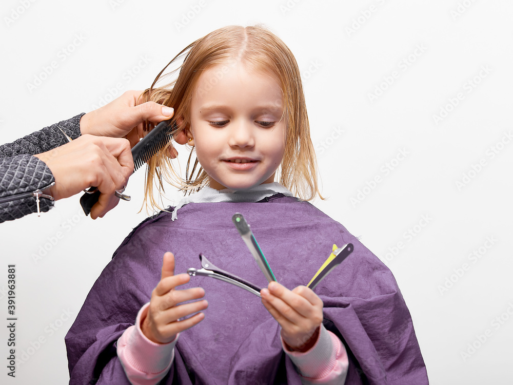 Foto de Hair cutting process. Beautiful little girl at the barber shop, hairdresser making a