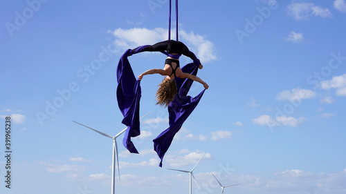 professional aerial gymnast performs a beautiful pose against the background of windmills