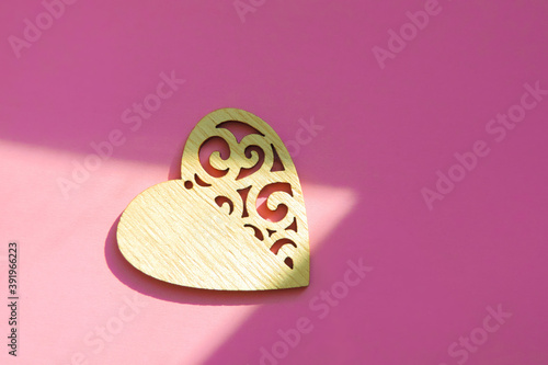 carved wooden heart on pastel pink background in cone-shaped natural sunlight stream, shadow and light concept, contrast. Copy space, flat lay, minimalism
