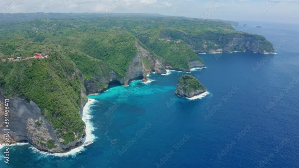 Aerial view of a beautiful scenic Kelingking Beach with a steep cliff and a cape covered with dense green vegetation washed by turquoise sea water on a sunny warm summer day. Aerial view of a beautiful scenic Kelingking Beach with a steep cliff and a cape covered with dense green vegetation washed by turquoise sea water on a sunny warm summer day.