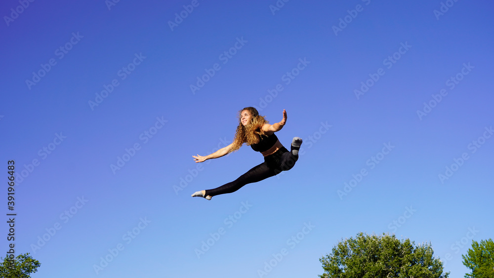 Beautiful girl jumping on a trampoline with hair fluttering in the wind against the background of the blue sky.