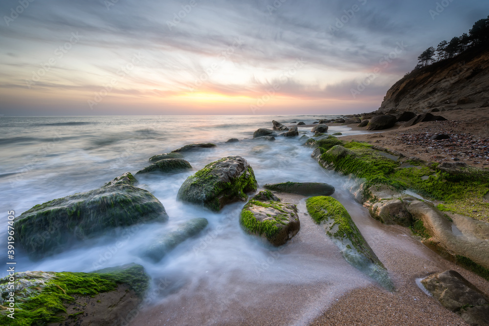 Amazing long exposure seascape with rocky beach at sunrise