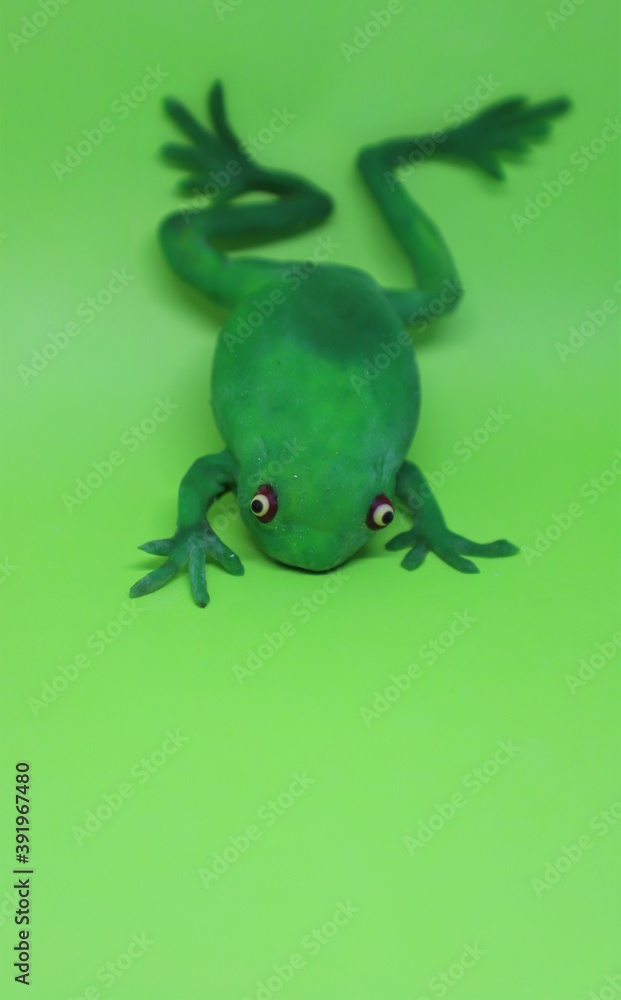 Fototapeta premium A green plastic toy frog isolated on a lime green background with text space 