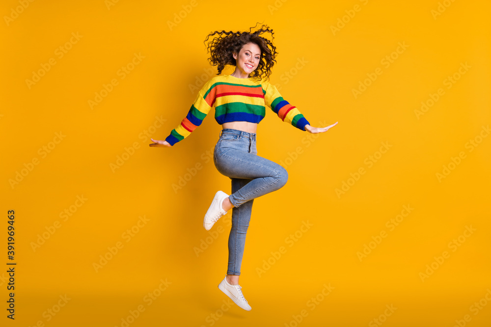 Full length photo of jumping lady wearing casual colorful sweater dancing pointing standing one leg isolated yellow color background