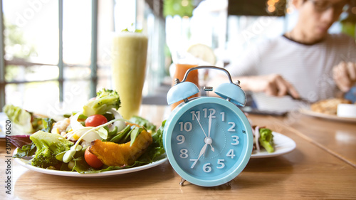 Selective focus of blue clock and breakfast time, alarm clock ntermittent fasting as a healthy and balanced breakfast
