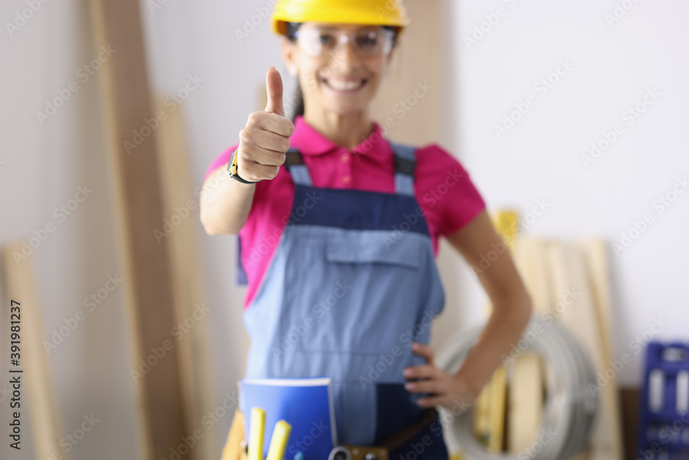 Smiling woman in construction overalls showing her thumb closeup. High-quality construction works concept Smiling woman in construction overalls showing her thumb closeup. High-quality construction works concept