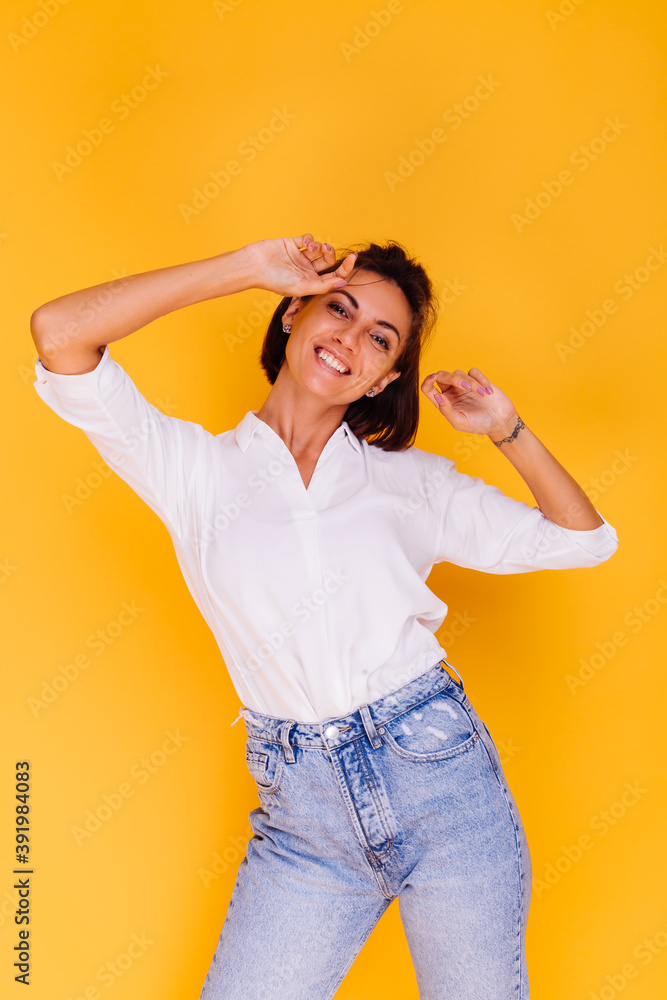 Studio shot of happy caucasian woman short hair wearing white shirt and denim pants posing on yellow background. Female in stylish casual clothes. Studio shot of happy caucasian woman short hair wearing white shirt and denim pants posing on yellow background. Female in stylish casual clothes.