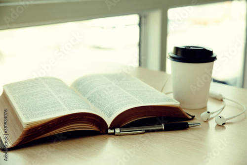 Open book with cup of coffee,pen,Earphone on wooden desk