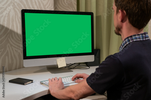 A man works in front of a computer with a green screen.