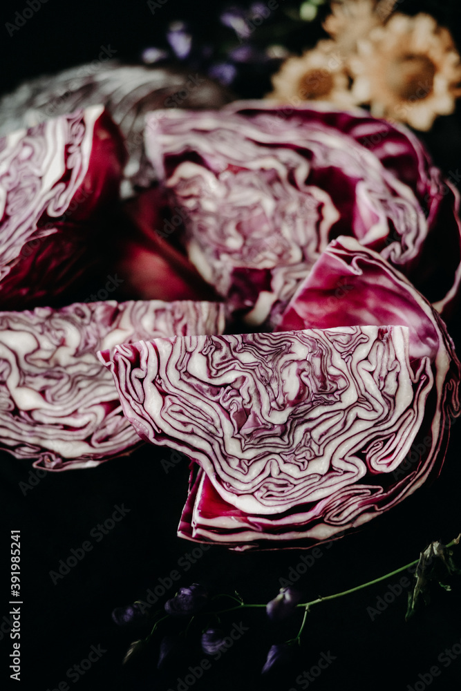 Obraz premium red cabbage on a dining table covered with a black tablecloth. still life with cabbage and flowers in rustic style. making blaukraut. flowers and leaves of red cabbage on the table
