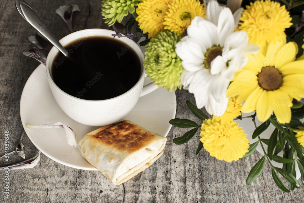 On a wooden table, a white Cup of coffee sits next to a bouquet of chrysanthemum flowers. Concept of rest and good morning On a wooden table, a white Cup of coffee sits next to a bouquet of chrysanthemum flowers. Concept of rest and good morning