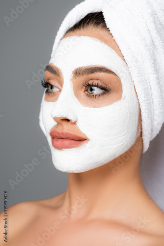 woman with towel on head and clay mask on face isolated on grey