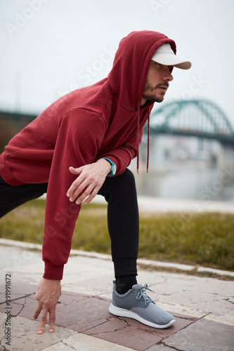 Athletic sporty man training in hoodie sweatshirt in urban city park.