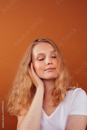 young pretty girl with blond curly hair posing cheerful on brown background, lifestyle people concept