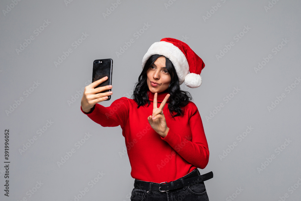 Young pretty woman in santa hat take selfie on the phone isolated on gray background Young pretty woman in santa hat take selfie on the phone isolated on gray background