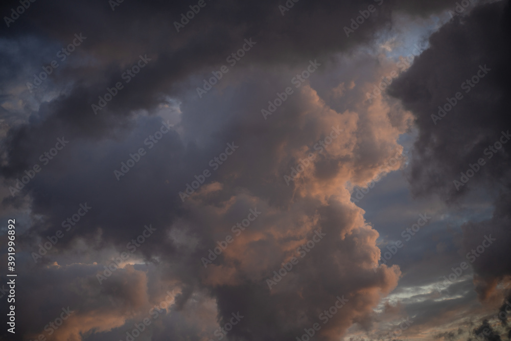 Silhouettes of epic stormy dark blue clouds with a gap of pink-orange light in a thunderstorm