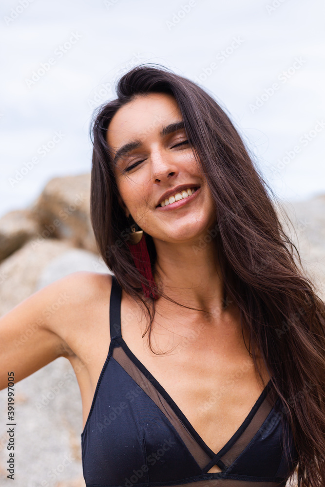 Portrait of happy slim stylish woman on rocky beach at sunset   