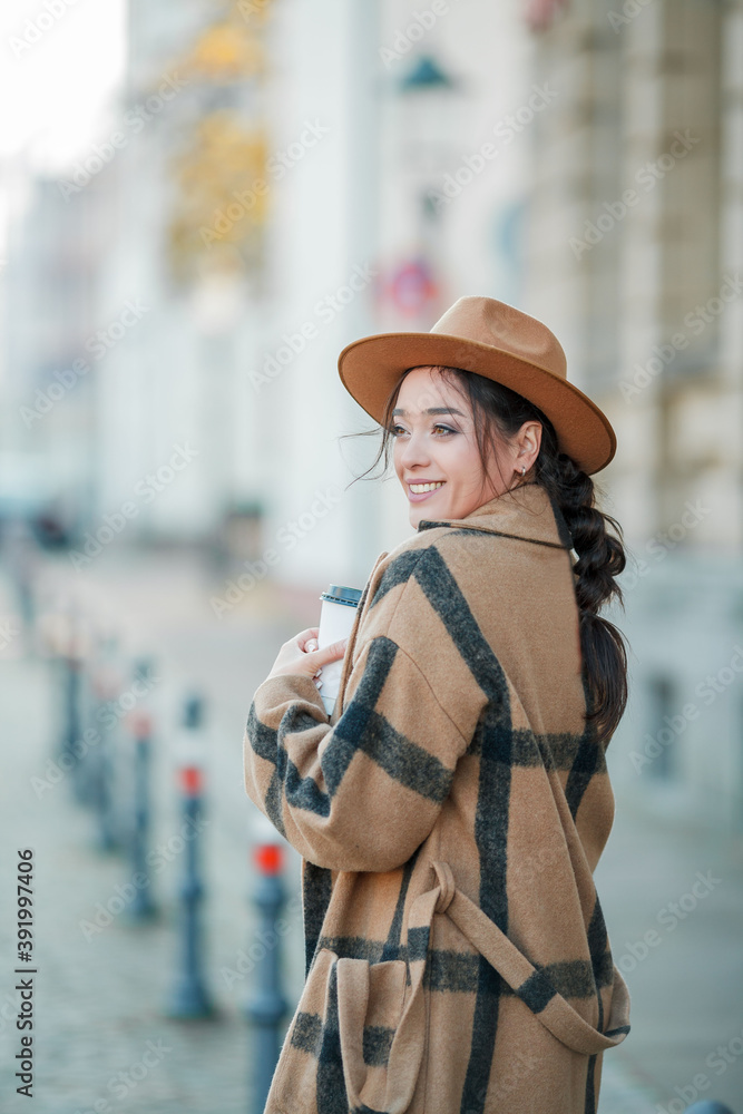 Beautiful young woman in a hat with coffee walks in a european city