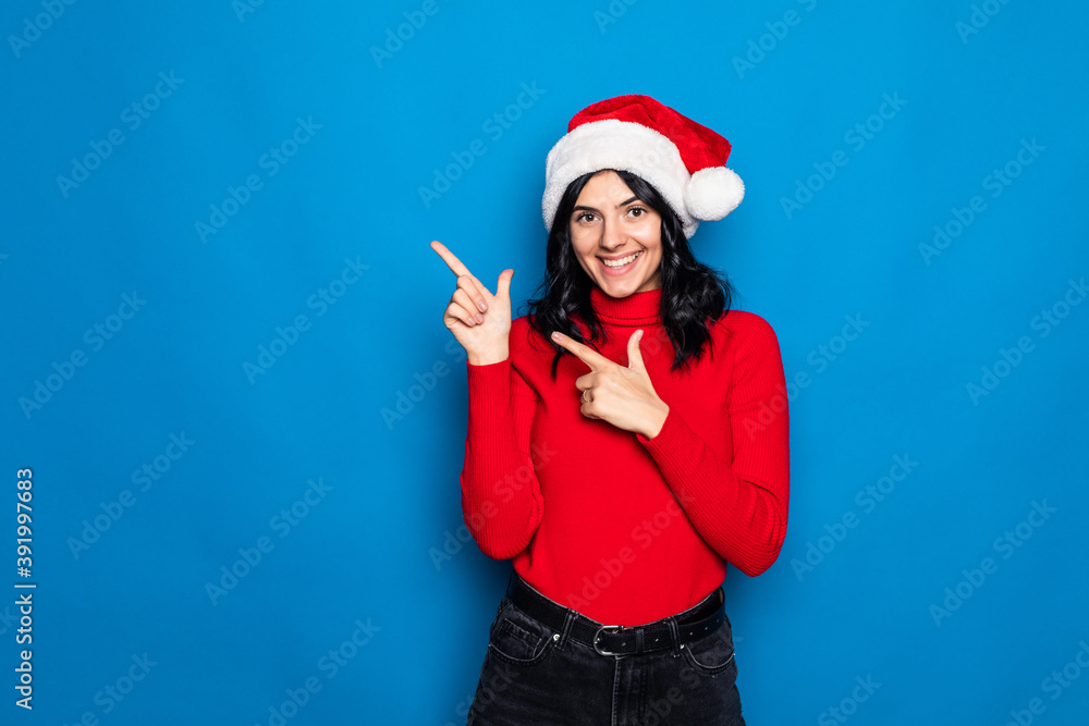 Woman with christmas hat pointing to the side to present a product isolated on blue background Woman with christmas hat pointing to the side to present a product isolated on blue background