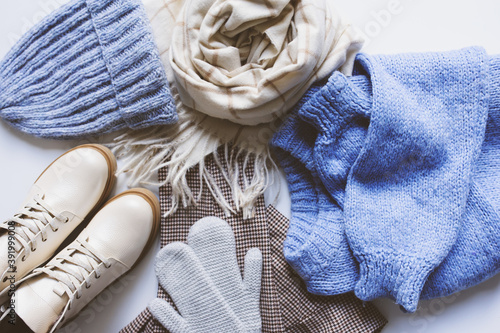 stylish modern winter or fall woman clothes set top view. Trendy shoes, sweaters and accessories in beige and blue tones with Christmas lights and autumn leaves.
