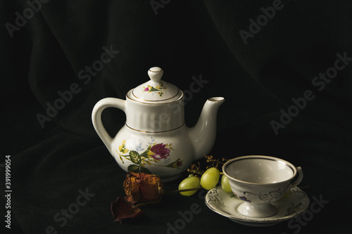 Still life on a black background, composition with a dead rose, grapes and porcelain teapot