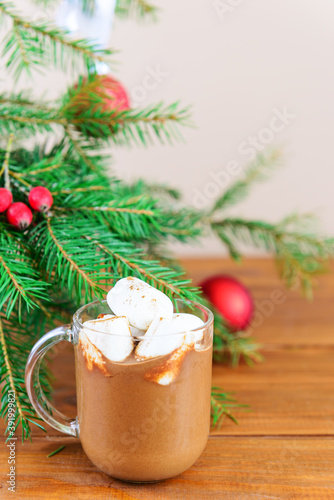 Hot chocolate with marshmallows and cinnamon in a glass mug on the background of a Christmas tree.