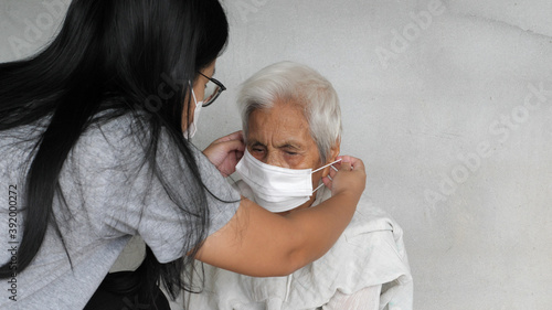 Asian grandchild woman wearing a white face mask to old grandmother prevent from covid 19. isolated concrete grey wall background. Rural lifestyle and health care concept.